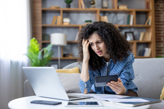 Stressed young woman managing home budget using calculator and laptop