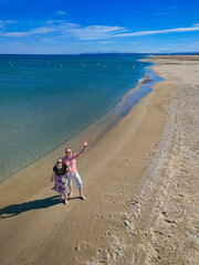 Happy married couple waves at camera on Port-la-Nouvelle beach, Mediterranean France. Perfect for travel romance, vacation lifestyle, coastal tourism, and relationship themes.