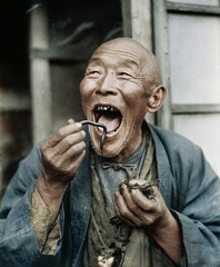 An elderly man from the Far East expresses joy as he is about to eat an earthworm.