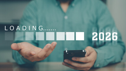 A man holds a smartphone with a futuristic loading bar labeled "2026", symbolizing progress, transition, and digital readiness for the next year. New year 2026.