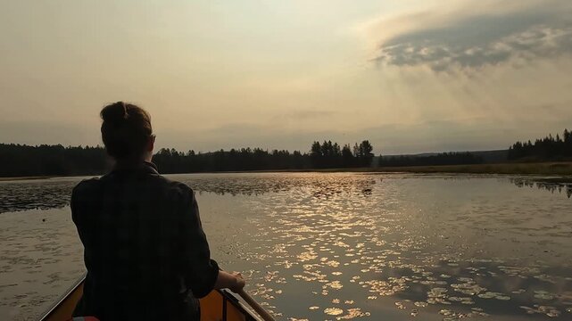 Cinematic 4K view in Temagami, showing a Caucasian woman paddling a canoe across calm water