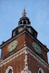 Obraz premium Historic brick clock tower with green dials and ornate spire rises against clear blue sky, symbolizing tradition, time, and architecture