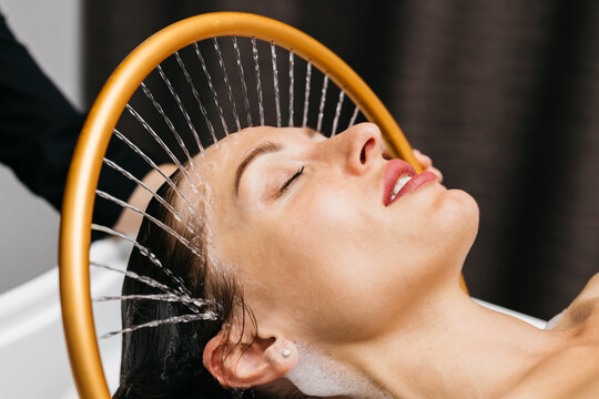 Woman enjoying hydromassage therapy with water cascading over her head in a serene spa environment, promoting relaxation and rejuvenation through aqua massage techniques