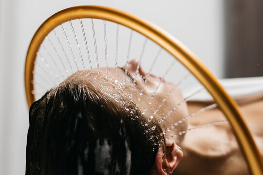 Woman enjoying hydromassage therapy with water cascading over her head, surrounded by a serene spa environment, emphasizing relaxation and rejuvenation in aqua massage experience