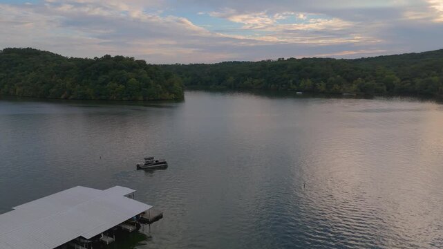 aerial spinning flyover of a lake flanked by trees and docks tilting up to the skyline while a boat passes by