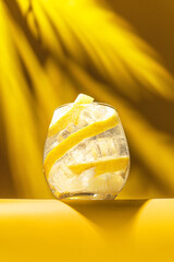 Refreshing cocktail with lemon zest and ice on yellow background