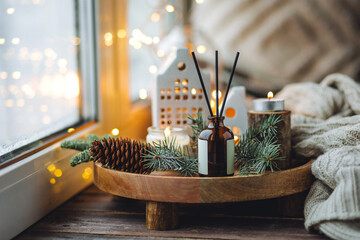 Natural Christmas essential oil, home aroma diffuser. Burning candles, branches of fir tree. Cinnamon, vanilla smell. Aromatherapy, cozy atmosphere, holiday festive mood. Close up macro, wooden table