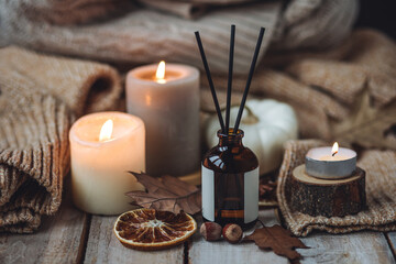 Hello autumn, cozy slow living. Pumpkin, aromatic candle, warm sweaters, dry fall leaves, cinnamon, anise in golden lights with bokeh on white wooden background. Thanksgiving apartment decor