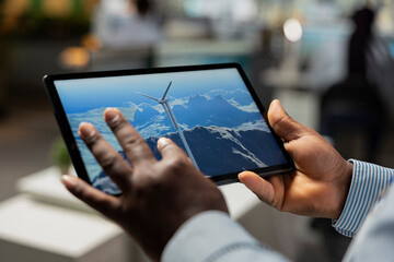 Close up of engineer in office using tablet to analyzes wind turbine and improve renewable energy efficiency. RD professional uses CAD app on device to upgrade windmill, boosting clean energy output