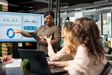 Group of businesswomen meeting in the office to align performance objectives with project indicators surrounded by reports and digital tools. Ambitious staff driving collective success.