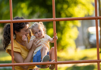 Little girl climbing bars in park with help from mom