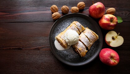 Obraz premium delicious apple strudel with ice cream on a black plate surrounded by walnuts and fresh apples on a dark wooden background with space for text