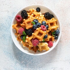 Tiny Mini waffles waffles with berries in a white bowl on a light background. Delicious breakfast