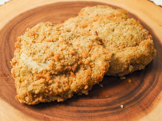 Breaded chicken breast fillet on a wooden board. Classic poultry product. Uncooked meat covered with golden breadcrumbs.