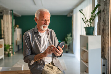 Senior man using smart phone and smiling at home