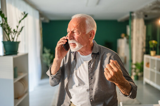 Senior man getting angry while talking on mobile phone at home