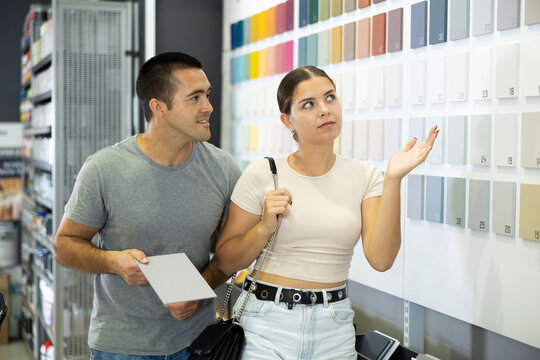 Couple standing next to display case featuring array of paint and varnish materials, discussing and selecting best cover option. Repair and construction items, paint and varnish products, supermarket - Powered by Adobe