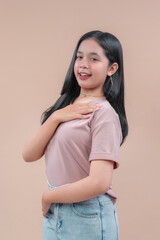 Obraz premium Asian young woman with long black hair wearing casual t-shirt and denim jeans, smiling with one hand on chest, showing confident and friendly pose against beige background.