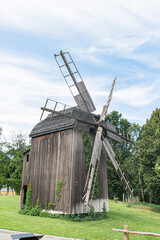 Worn wooden Central European windmill in a grassy area, set against trees and clear sky. a