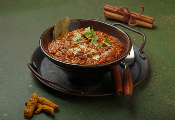 Steaming bowl of Dal makhani, a traditional indian lentil dish, garnished with fresh coriander and cream, presented on a rustic metal tray with turmeric and cinnamon on dark green background
