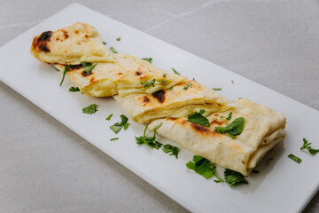 Grilled lavash rolls with melted cheese and herbs on a white ceramic plate