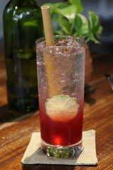 glass of red and clear liquid with a bamboo straw and lime slice