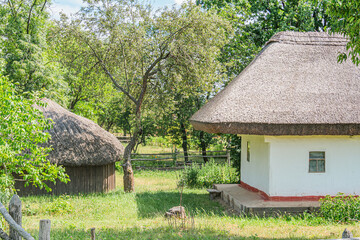 Fototapeta premium Ancient Central European village, quaint rural scene, traditional hut or house, natural materials straw, grass, covered area, wooden bench, lush green setting possible springsummer, trees, candi