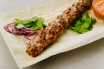 Grilled lamb lula kebab with onion, herbs, and spicy sauce on lavash bread