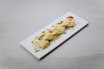 Grilled lavash rolls with melted cheese and herbs on a white ceramic plate