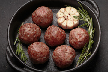 Raw meatballs seasoned with rosemary and garlic are waiting to be cooked in a cast iron pan top view on rustic dark background