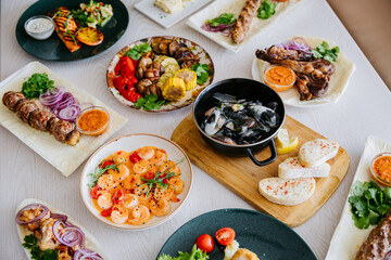 Top view of assorted grilled meats, seafood, and side dishes on a restaurant table