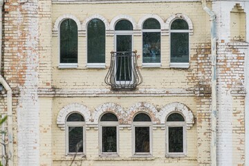 Historical multi-storied building, possibly stone or concrete, with grouped windows and decorative arches in an urban European setting, under soft lighting