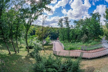 Wooden paviliondeck amidst green trees and plants in a modern urban setting, under clear blue sky with scattered white clouds a