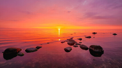 Sunset over calm sea with stones in water, colorful sky and reflection