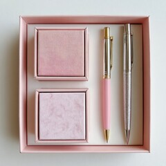 Pink gift set of stationery items.  Two small, square, light pink boxes sit beside each other in a larger, square, light pink gift box. Two pens, one pink and one silver, lie between the boxes