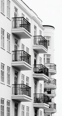 Exterior view of a multi-story apartment building, featuring numerous balconies and windows.  Clean lines and a minimalist aesthetic,  black metal railings contrast with the white facade