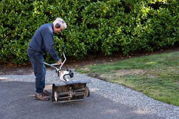 Senior man pulling start cord on gas powered dethatching machine, wearing hearing protection ear...