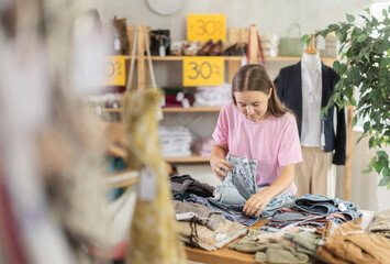 Teenage girl buyer choosing jeans in clothing store