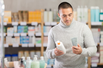 In drug store, man examine emollient cream packaging, buy product. Client study composition of pill in detail. Checking for absence of GMOs, age restrictions and recommendations for use