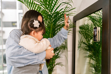 Mother holding her baby while pointing at mirror with smartphone attached