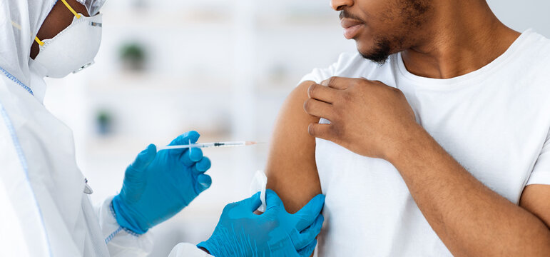 Vaccination and immunization concept. Closeup of young african american man receiving vaccine shot during coronavirus pandemic. Closeup of doctor in PPE making injection in shoulder for male patient