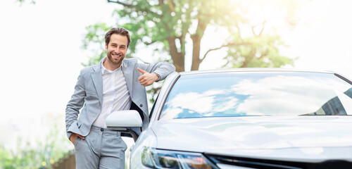 Auto dealer in car dealerships, transport rental service. Agent approving to client, rent vehicle in rental office. Millennial attractive european guy in suit stands near new white car, shows thumb up