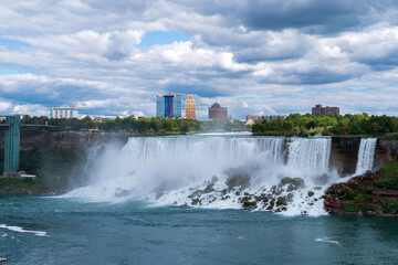 Stunning view of the American Falls at Niagara, with cascading water, mist, and a dramatic cloudy sky against the city skyline.