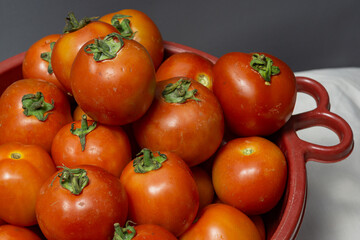 A red basket full of fresh, ripe red tomatoes from the market.