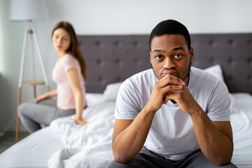 Sad black man sitting on bed, deep in thought, overwhelmed with family problems, his dissatisfied...