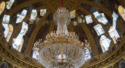 Obraz premium Low-angle view of a grand chandelier in an ornate, domed room with stained glass windows