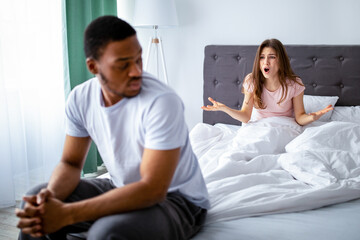 Angry young woman shouting at her black husband, having conflict on bed at home, copy space....