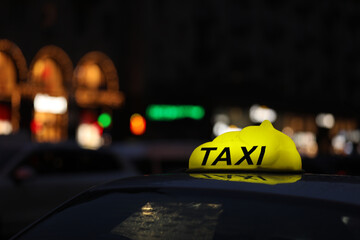 Taxi car with yellow checkered sign on city street in evening, closeup