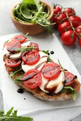Delicious sandwich with mozzarella cheese, balsamic sauce, tomatoes and arugula on grey table, closeup