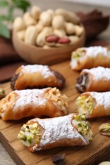 Delicious cannoli with ricotta cheese, peanuts, pistachios, chocolate and powdered sugar on wooden table, closeup